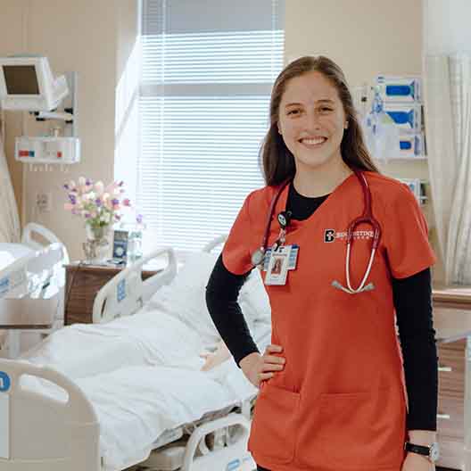 A nursing student poses for a photo in the nursing lab
