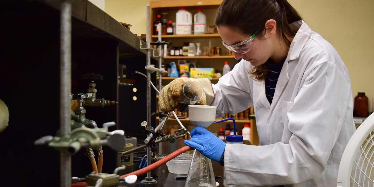 A female student pours from a beaker into a flask in Chemistry class