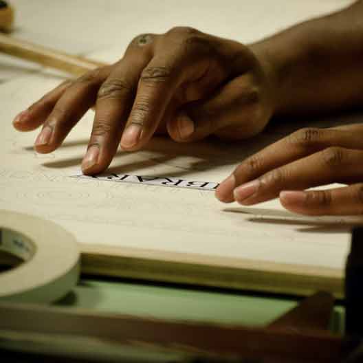 A student's hands working at a drafting table in Architecture class