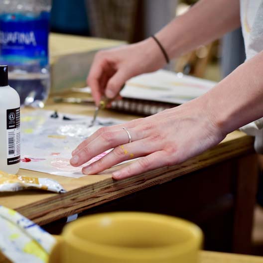 A student's hands work with art supplies at a table