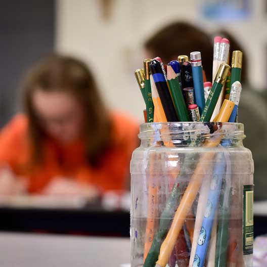 A jar of pencils, with a students at work in the background